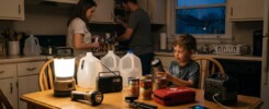Family organizing water, canned food, lighting, a radio, first-aid supplies and a portable power station for a household power outage.